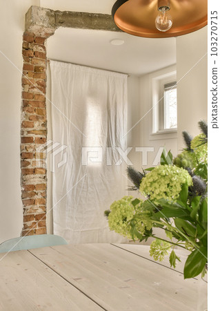 a dining room with a table and flowers in the vase on the wooden floor next to an exposed brick wall a dining room with a table and flowers in the vase on the wooden floor next to an exposed brick wall 103270715