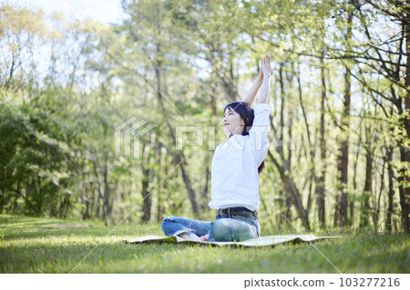 A Japanese woman who enjoys yoga while relaxing in a natural early summer forest 103277216