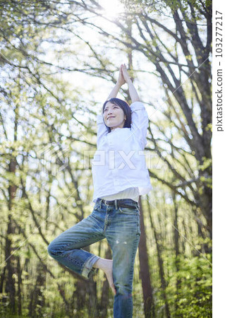 A Japanese woman who enjoys yoga while relaxing in a natural early summer forest 103277217