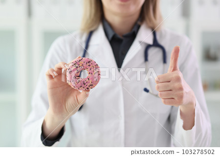 Doctor holds sweet donut in hand showing thumb up gesture 103278502