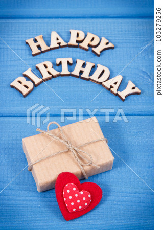 Wrapped gift with ribbon for birthday. Inscription happy birthday on boards Wrapped gift with ribbon for birthday. Inscription happy birthday on boards 103279256