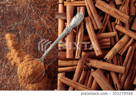 Cinnamon powder in a spoon and cinnamon sticks on a brown background. Cinnamon powder in a spoon and cinnamon sticks on a brown background. 103279588