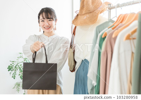 A smiling female clerk at a select shop/clothing store handing a paper bag to a customer 103280958