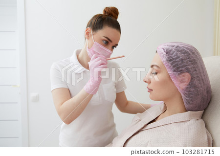 Cosmetologist drawing mark on client face to prepare for rejuvenation treatment Cosmetologist drawing mark on client face to prepare for rejuvenation treatment 103281715