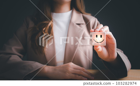 Businesswoman choosing on the happy Smile face icon give satisfaction in good service, Smile face and sad face on wooden block cube for positive mindset selection. Mental health and emotional state 103282974