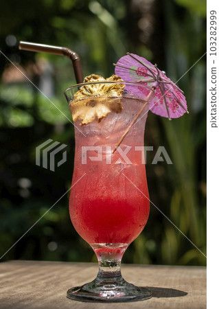 tropical singapore sling cocktail in tall glass at garden bar 103282999