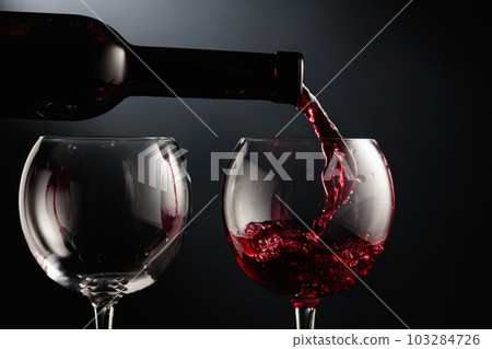 Pouring red wine into a wine glass. Pouring red wine into a wine glass. 103284726