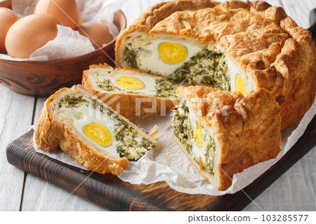 Portioned traditional Italian Easter cake or tart with spinach, ricotta and whole eggs closeup on the wooden board. Horizontal Portioned traditional Italian Easter cake or tart with spinach, ricotta and whole eggs closeup on the wooden board. Horizontal 103285577