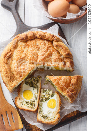 Homemade Torta Pasqualina is a traditional Ligurian Easter pie made with greens, ricotta, egg, and cheese closeup on the wooden board. Vertical top view Homemade Torta Pasqualina is a traditional Ligurian Easter pie made with greens, ricotta, egg, and cheese closeup on the wooden board. Vertical top view 103285600