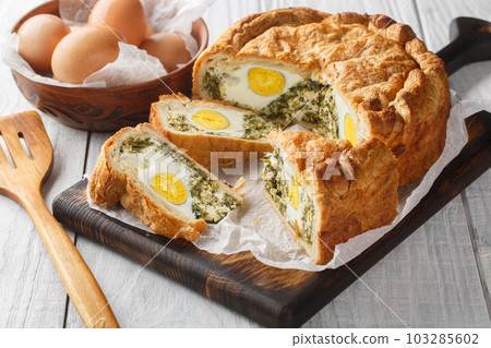 Torta Pasqualina is an traditional Italian Easter speciality made of puff pastry, ricotta cheese, spinach and eggs closeup on the wooden board. Horizontal Torta Pasqualina is an traditional Italian Easter speciality made of puff pastry, ricotta cheese, spinach and eggs closeup on the wooden board. Horizontal 103285602