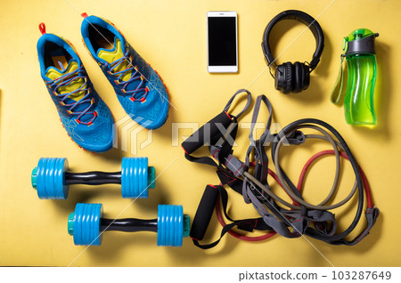 Running shoes and a variety of cardio and fitness items. Fitness at home on the mat. Objects on a yellow background. Running shoes and a variety of cardio and fitness items. Fitness at home on the mat. Objects on a yellow background. 103287649