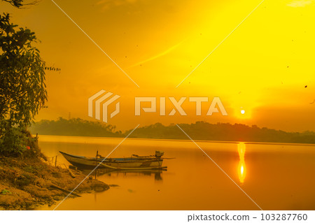 Traditional boat moored on the calm and tranquil lake during sunrise in Jatibarang Dam, Semarang, Indonesia. Traditional boat moored on the calm and tranquil lake during sunrise in Jatibarang Dam, Semarang, Indonesia. 103287760