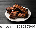 Freshly cooked pork ribs on a white round plate on a black wooden table in the background. Close-up 103287946
