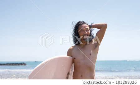 Long-haired middle male surfer holding a surfboard Long-haired middle male surfer holding a surfboard 103288326