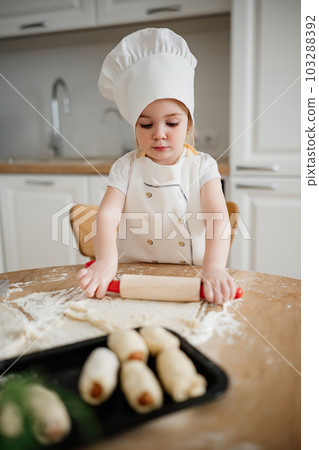 Adorable girl in chef hat and apron rolling out pastry dough 103288392