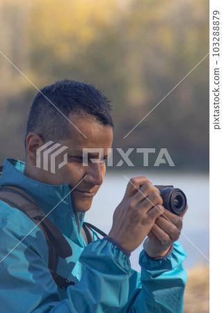 Portrait of traveler man at lake in autumn taking a photo with the digital camera 103288879