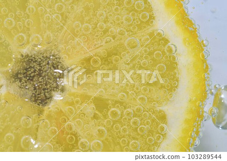 Slice of ripe lemon in water on white background. Close-up of lemon in liquid with bubbles. Slice of ripe citron in sparkling water. Macro image of fruit in carbonated water. 103289544