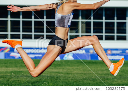close-up female athlete jumping triplejump in summer athletics championships on background green field close-up female athlete jumping triplejump in summer athletics championships on background green field 103289575