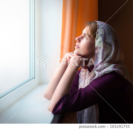 Girl praying by the window 103291735