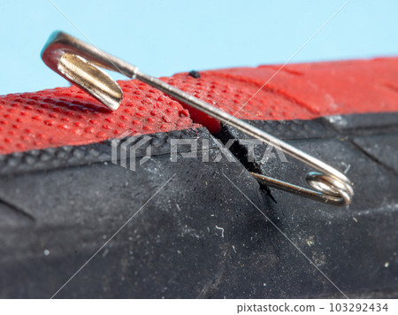 The bicycle tire is damaged by a safety pin, close up view. 103292434