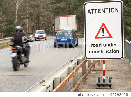 A sign beside road with traffic show warning message Road under construction. A sign beside road with traffic show warning message Road under construction. 103292438