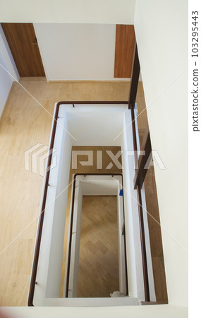 Hotel staircase with slightly curved architecture, windows and historic metal railing. Stairs are tiled and the handrail is supplemented with wooden handrail. There is also wood on walls and paneling. 103295443
