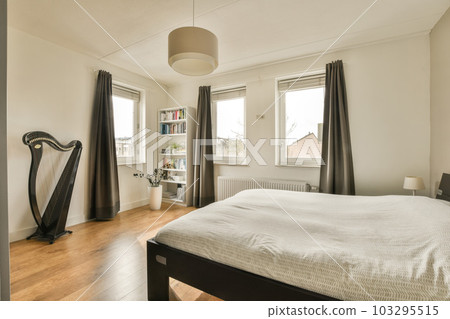 a bedroom with wood flooring and white sheets on the bed, there is a large black harp in the corner of the room 103295515