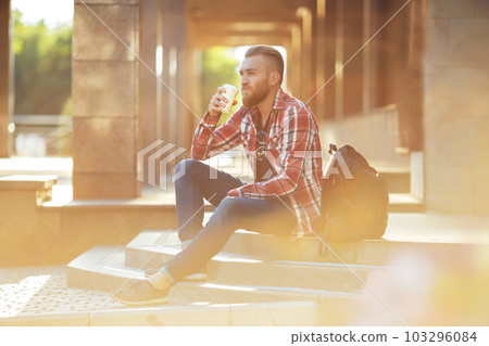 Handsome young man holding mobile phone and drinking coffee while sitting in the rest area. 103296084
