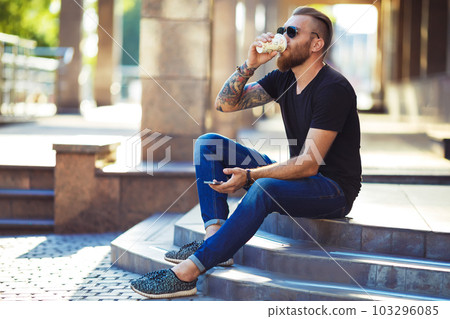 Handsome young man holding mobile phone and drinking coffee while sitting in the rest area. 103296085