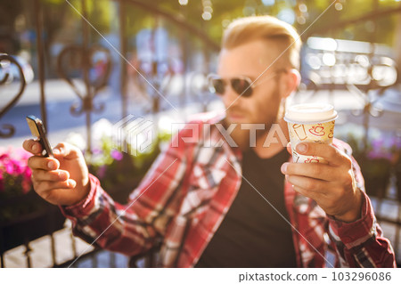 Handsome young man holding mobile phone and drinking coffee while sitting in the rest area. Handsome young man holding mobile phone and drinking coffee while sitting in the rest area. 103296086