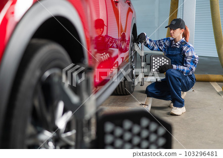 A female auto mechanic makes a camber. Woman working in a car service. A female auto mechanic makes a camber. Woman working in a car service. 103296481