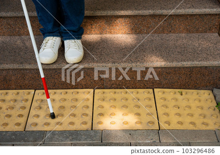 Close-up of female foot, walking stick and tactile tiles. Blind woman walking down stairs using a cane.  103296486
