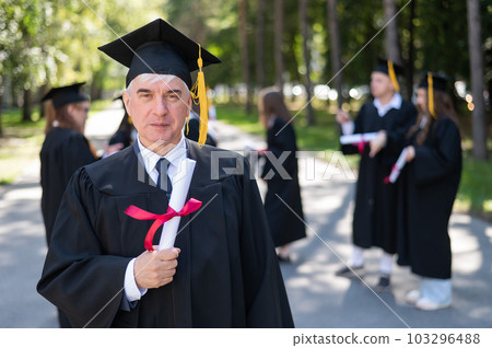 A group of graduates in robes outdoors. An elderly student rejoices at receiving a diploma. A group of graduates in robes outdoors. An elderly student rejoices at receiving a diploma. 103296488