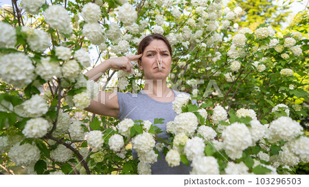 Unhappy woman with a clothespin on her nose on a walk in a blooming park. Unhappy woman with a clothespin on her nose on a walk in a blooming park. 103296503