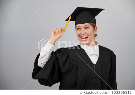 Smiling woman in graduation gown holding cap by tassel on white background.  103296511