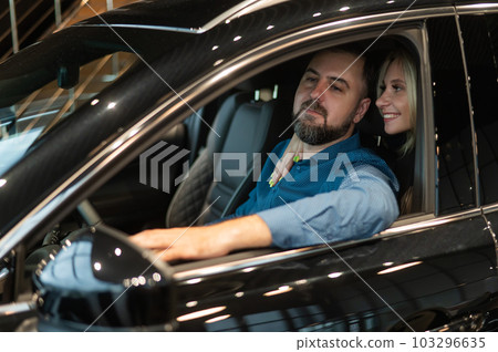 Happy married couple testing new car in car showroom. Happy married couple testing new car in car showroom. 103296635