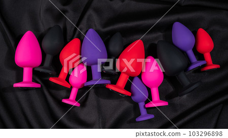 A set of silicone anal plugs in different colors and sizes on a black silk sheet. A set of silicone anal plugs in different colors and sizes on a black silk sheet. 103296898