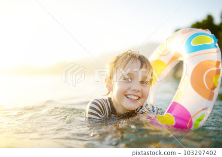 Little boy swimming with colorful floating ring in sea on sunny summer day. Cute child playing in clean water. Family and kids resort holiday during summer vacations. Little boy swimming with colorful floating ring in sea on sunny summer day. Cute child playing in clean water. Family and kids resort holiday during summer vacations. 103297402