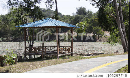 A gazebo or a hunt a place for relax and sit gather near the lake side and a pathway in a public park. A gazebo or a hunt a place for relax and sit gather near the lake side and a pathway in a public park. 103297746