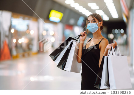 Fashionable woman in protective medical mask with shopping bags walking in the mall. Covid-19. Fashionable woman in protective medical mask with shopping bags walking in the mall. Covid-19. 103298286