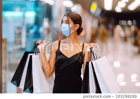 Fashionable woman in protective medical mask with shopping bags walking in the mall. Covid-19. 103298289