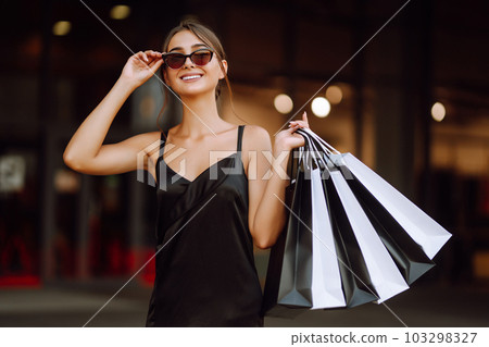 Fashion woman enjoying shopping. Elegant woman wears black dress holding black and white shopping bags. Fashion woman enjoying shopping. Elegant woman wears black dress holding black and white shopping bags. 103298327