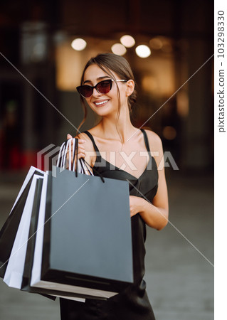 Fashion woman enjoying shopping. Elegant woman wears black dress holding black and white shopping bags. 103298330