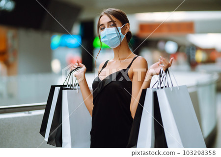 Fashionable woman in protective medical mask with shopping bags walking in the mall. Covid-19. 103298358
