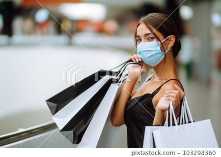 Beautiful fashionable woman in protective medical mask with shopping bags walking near mall. Covid-19. 103298360
