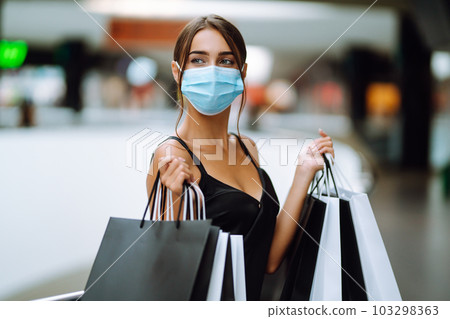 Fashionable woman in protective medical mask with shopping bags walking in the mall. Covid-19. Fashionable woman in protective medical mask with shopping bags walking in the mall. Covid-19. 103298363