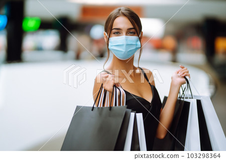 Beautiful fashionable woman in protective medical mask with shopping bags walking near mall. Covid-19. Beautiful fashionable woman in protective medical mask with shopping bags walking near mall. Covid-19. 103298364