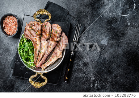Grilled Lamb mutton Chops steaks in a skillet with green salad. Black background. Top view. Copy space Grilled Lamb mutton Chops steaks in a skillet with green salad. Black background. Top view. Copy space 103298776