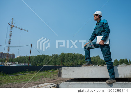 Caucasian male builder in hardhat holding laptop at construction site.  103299844