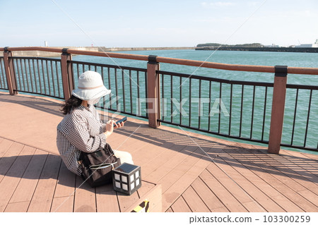 A woman operating a mobile phone at the beach on a trip A woman operating a mobile phone at the beach on a trip 103300259